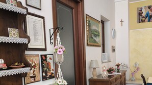 Una stanza con un armadio in legno, un certificato incorniciato, un pannello macramè, un tavolo con tovaglia a fiori e una sedia.