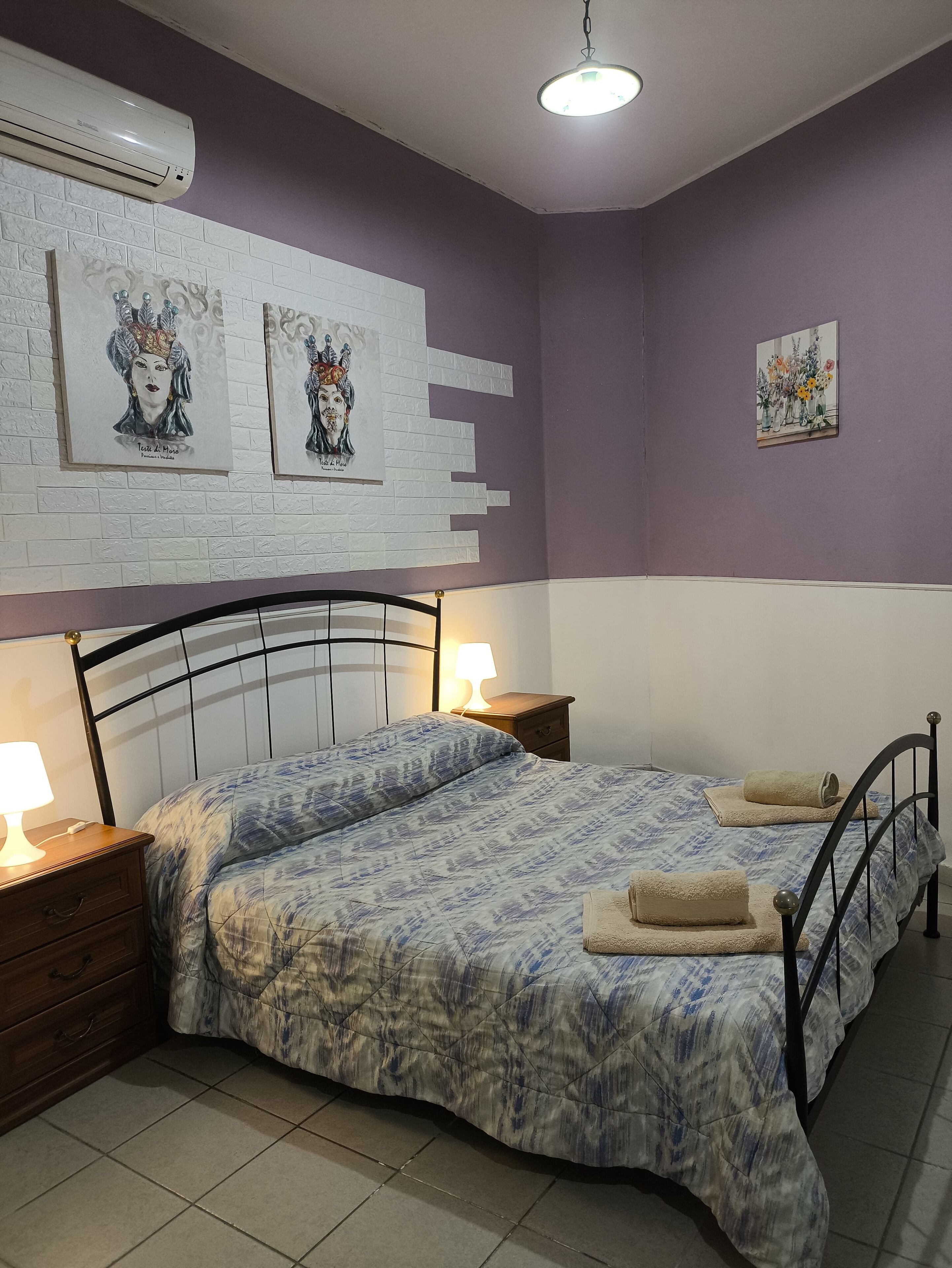 A bedroom with two beds, a nightstand, a lamp, and artwork on the wall.