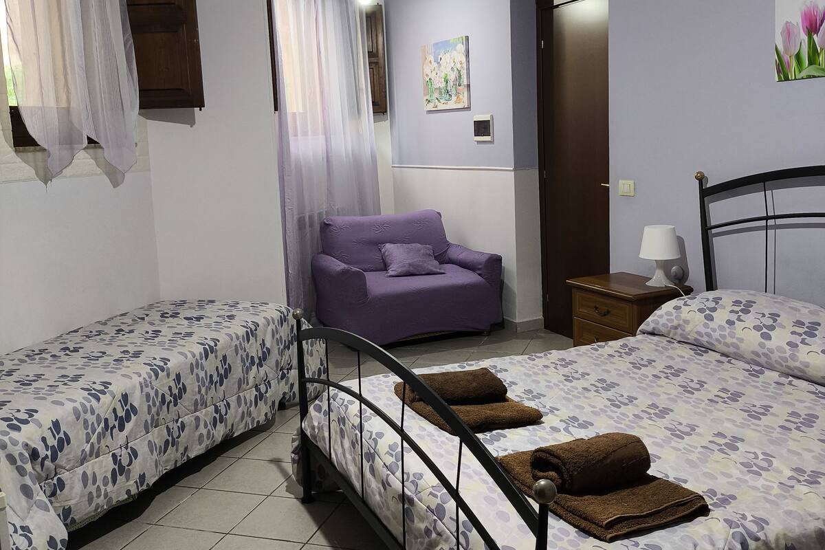 A bedroom with two single beds, a purple sofa, a nightstand, and a painting on the wall.