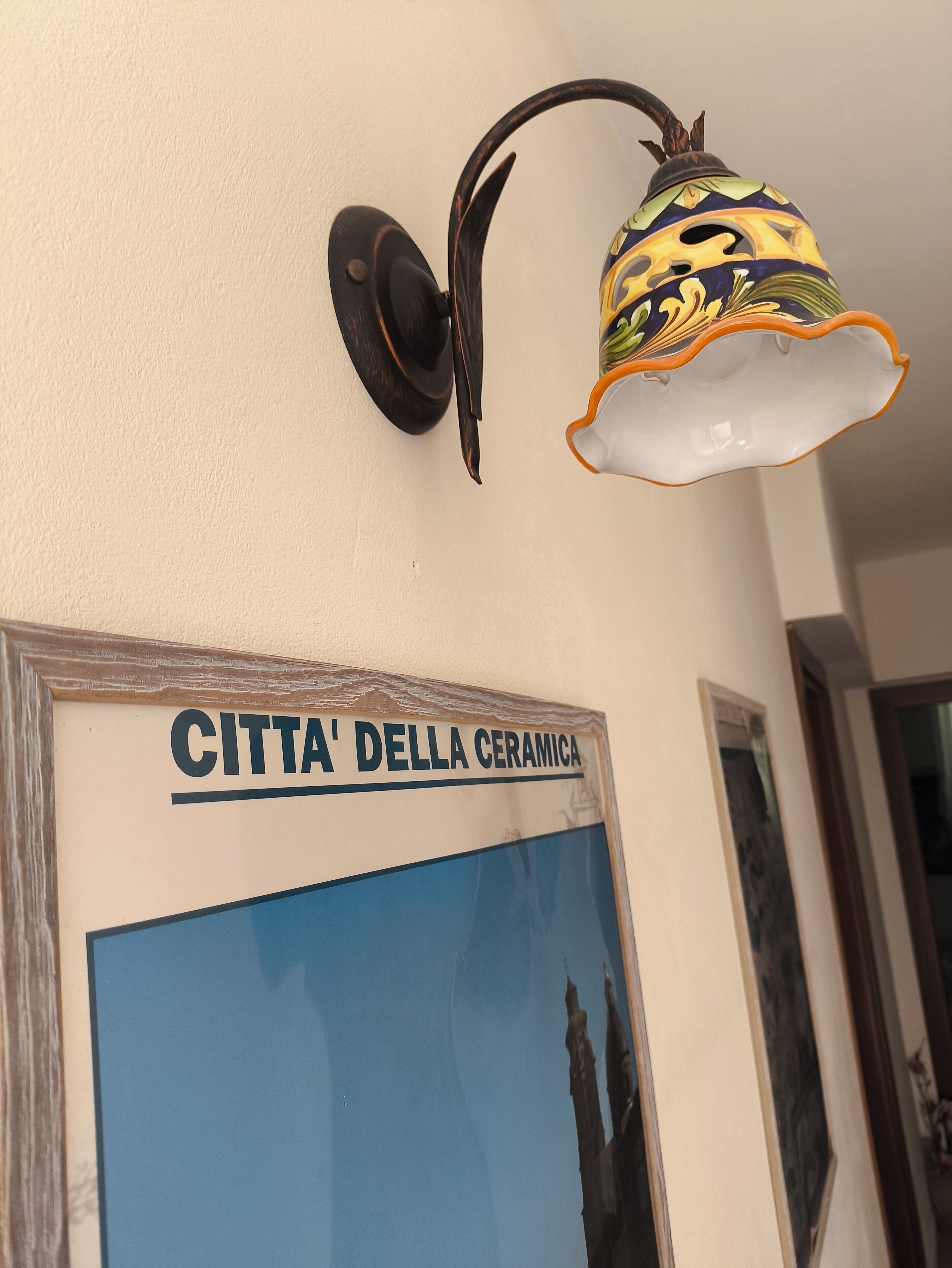 A wall-mounted light fixture with a ceramic design and a sign reading "CITTA' DELLA CERAMICA".