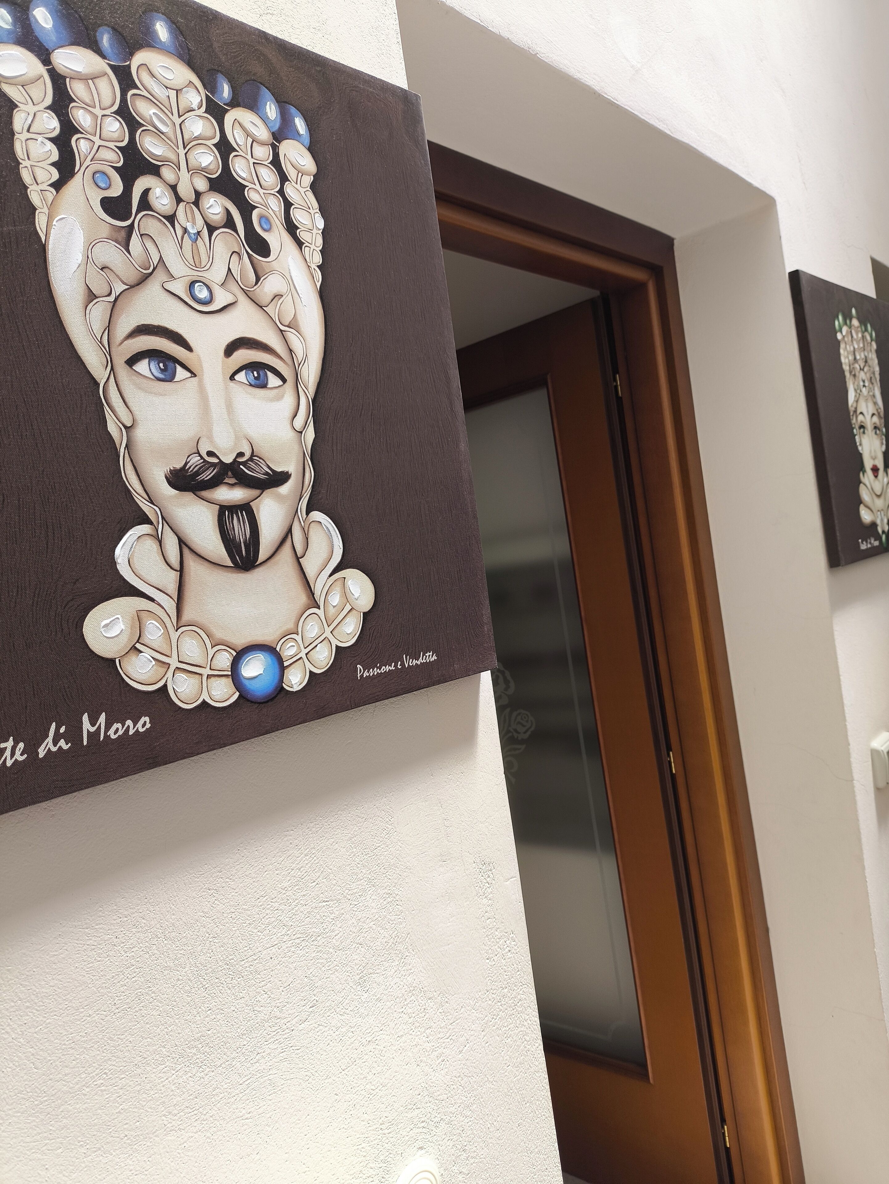 A wall with a framed artwork depicting a stylized face with a mustache and a blue gem.