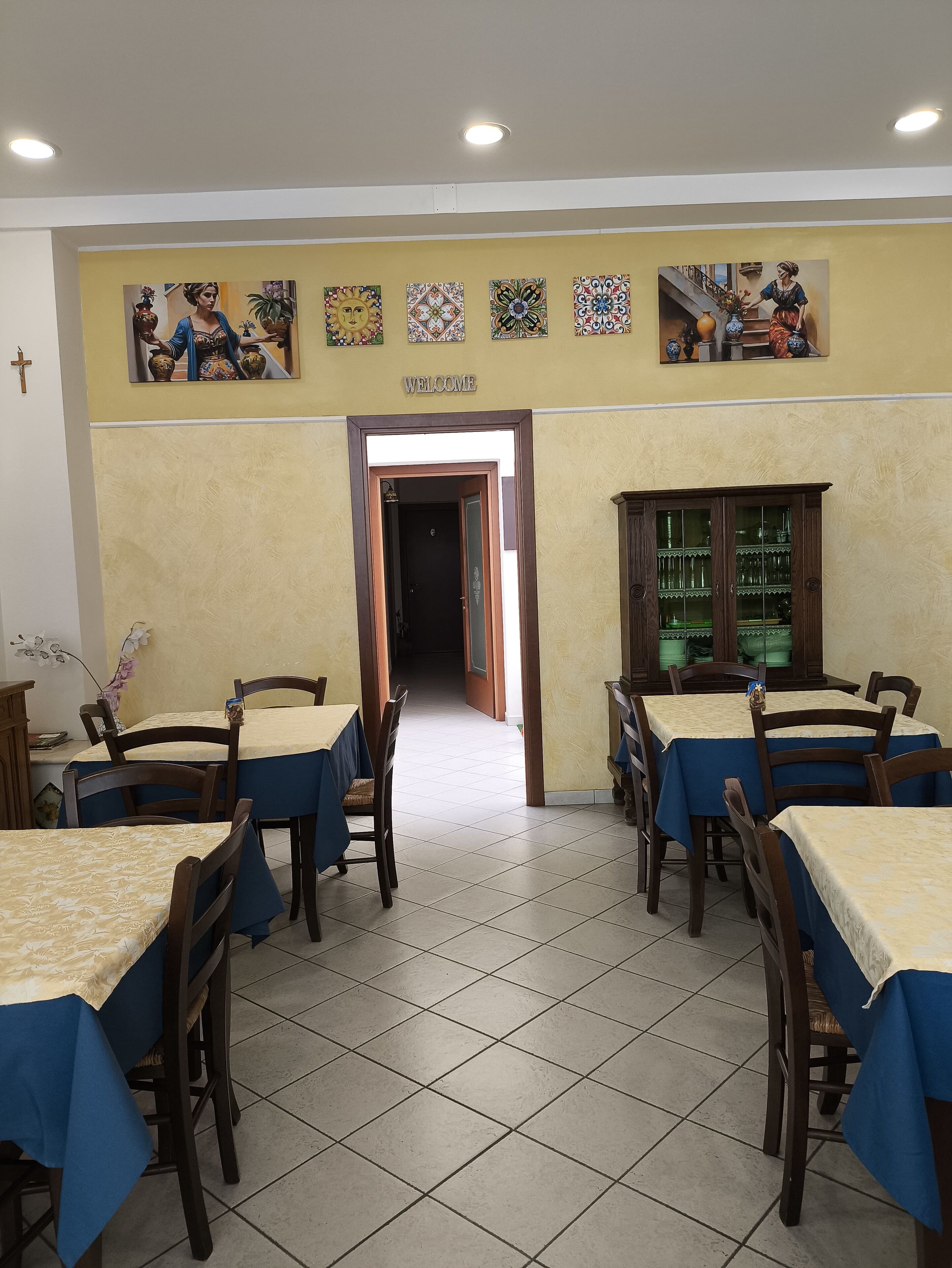 Comedor con mesas y sillas, un cartel que dice 'WELCOME' y decoración en la pared.
