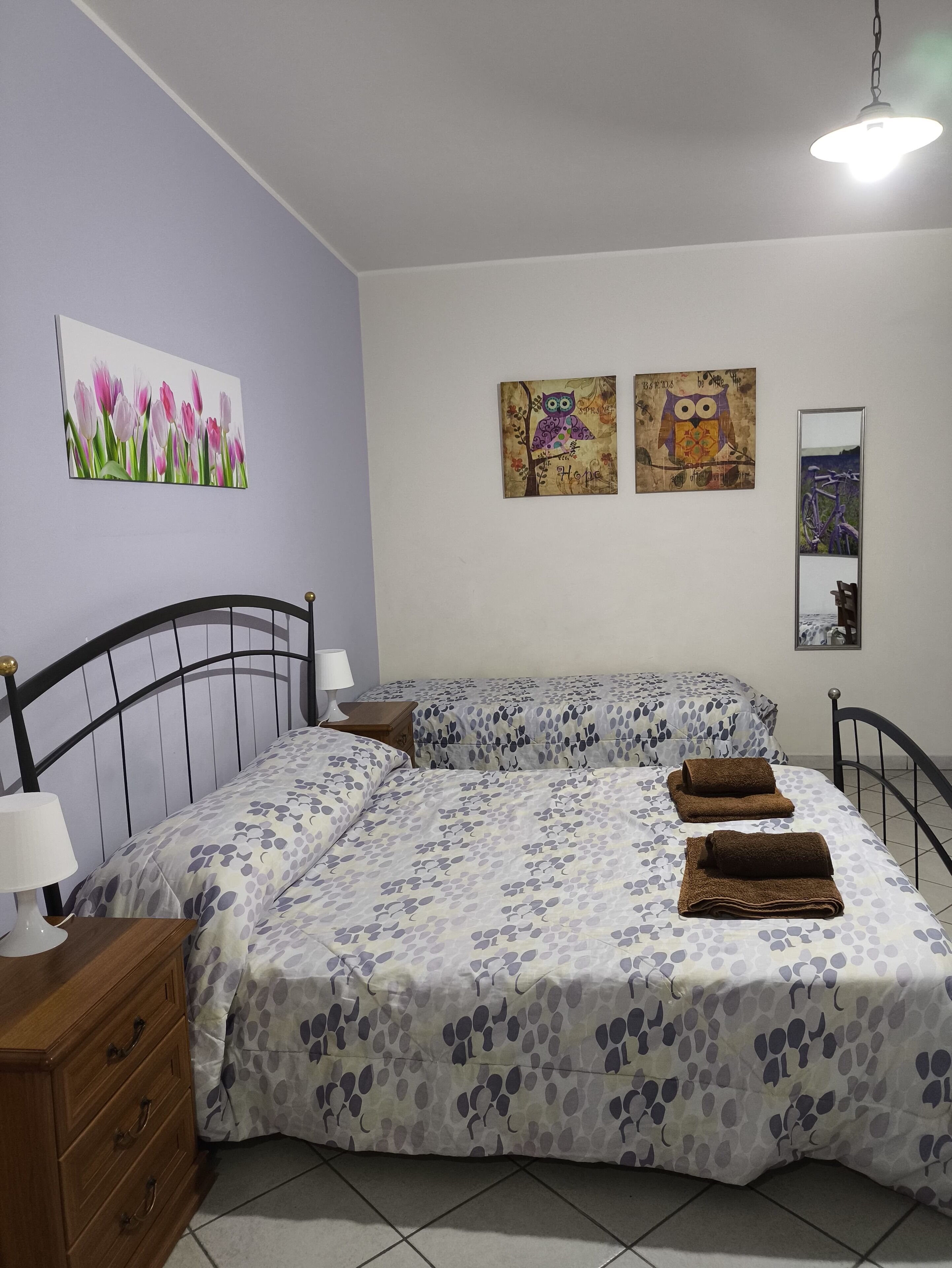 Une chambre avec deux lits, une table de chevet, une commode et des œuvres d’art murales.