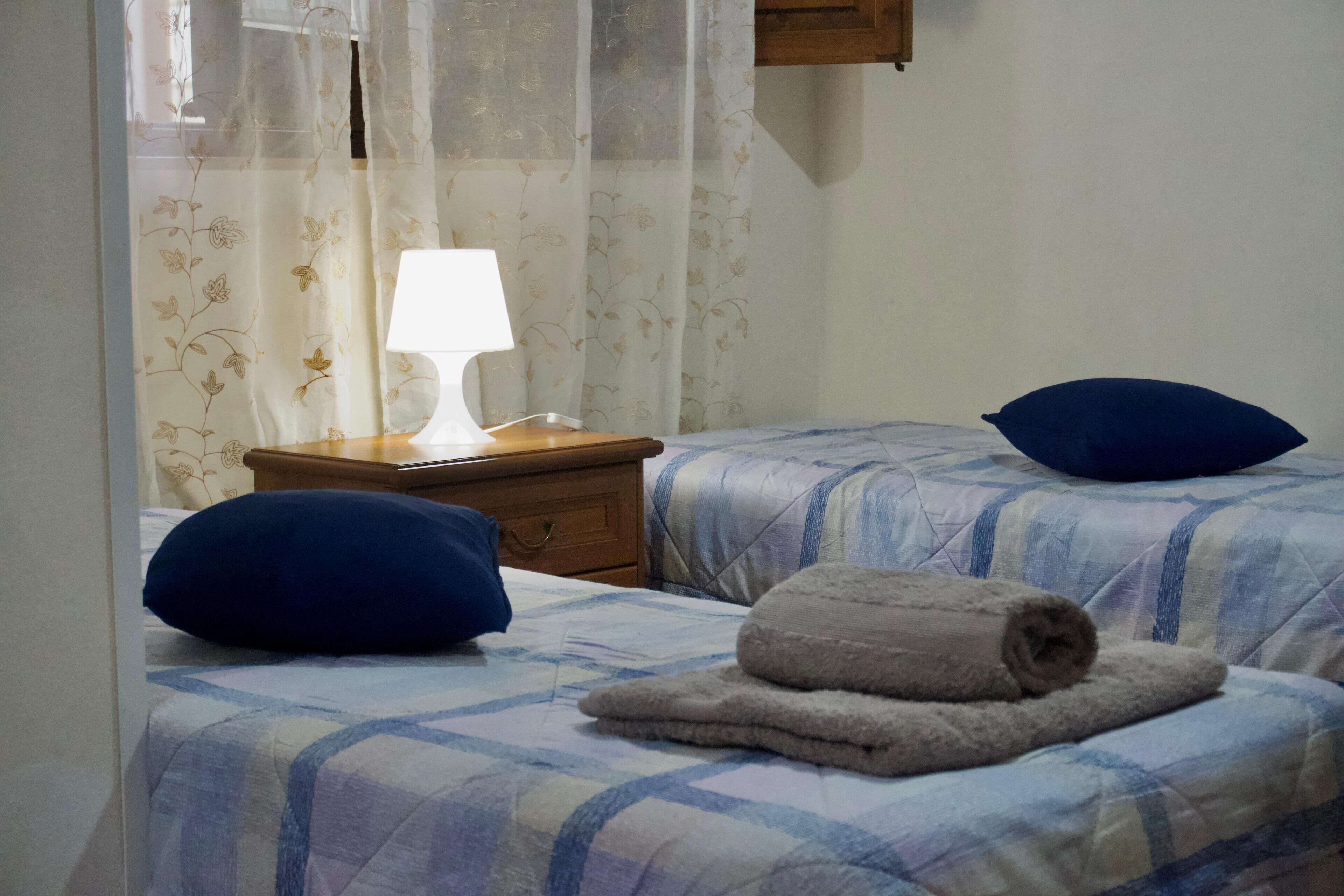 A bedroom with two beds, a nightstand, a lamp, and a window with floral curtains.