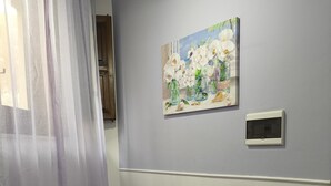 Una stanza con un divano viola, un quadro con dei fiori al muro e un termostato.