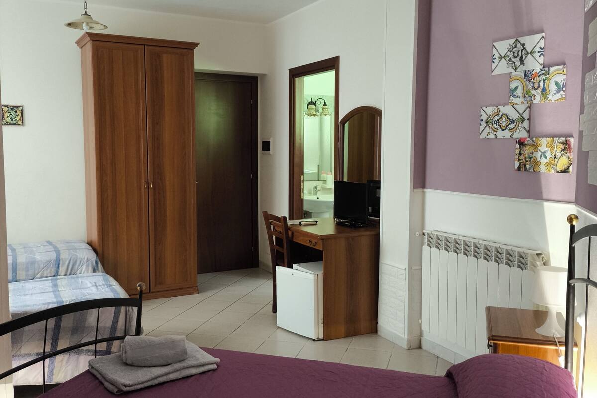 A bedroom with a bed, a desk, a wardrobe, and a radiator.