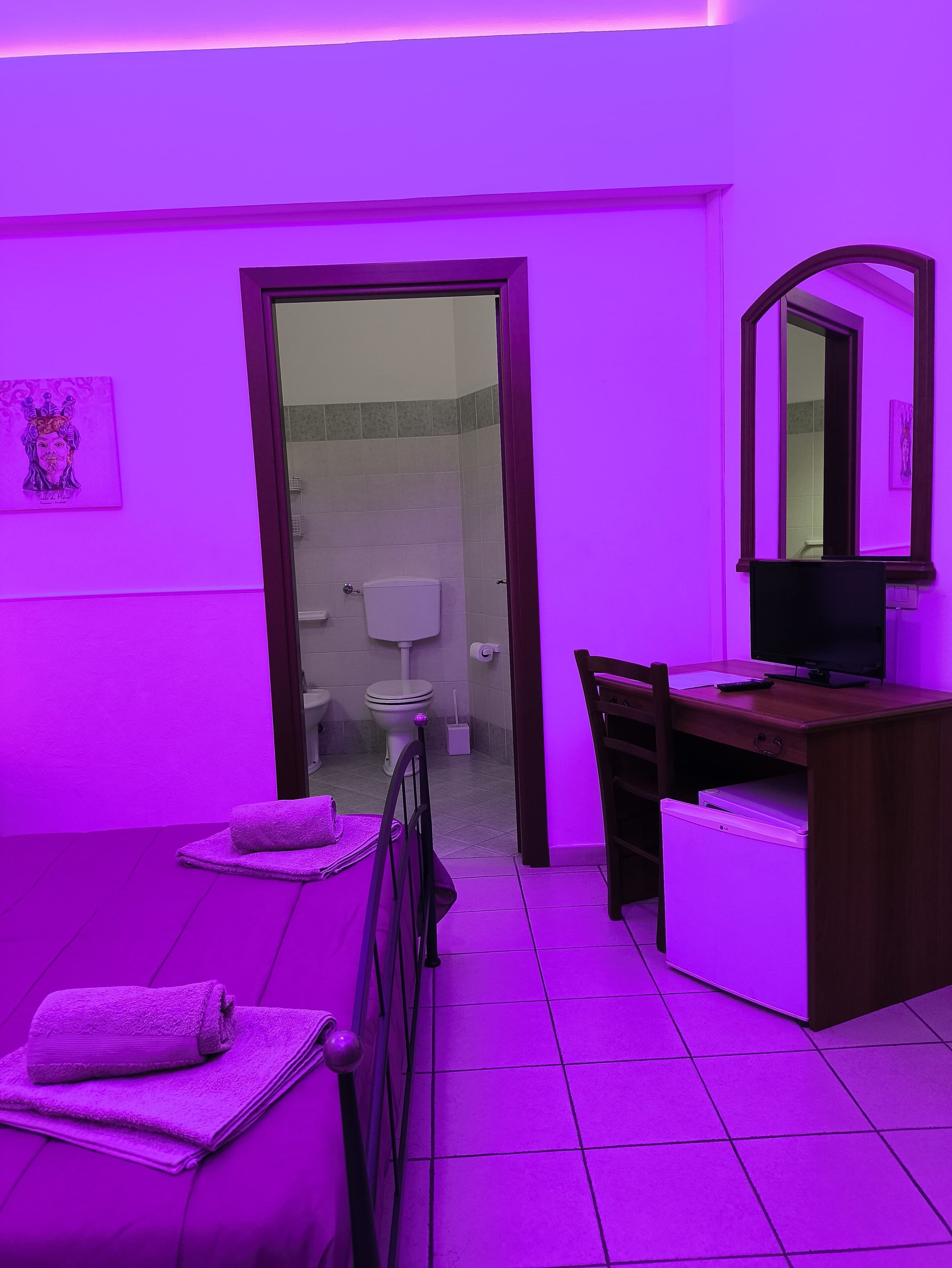Habitación con cama, escritorio, silla, televisión y baño visible a través de una puerta abierta.