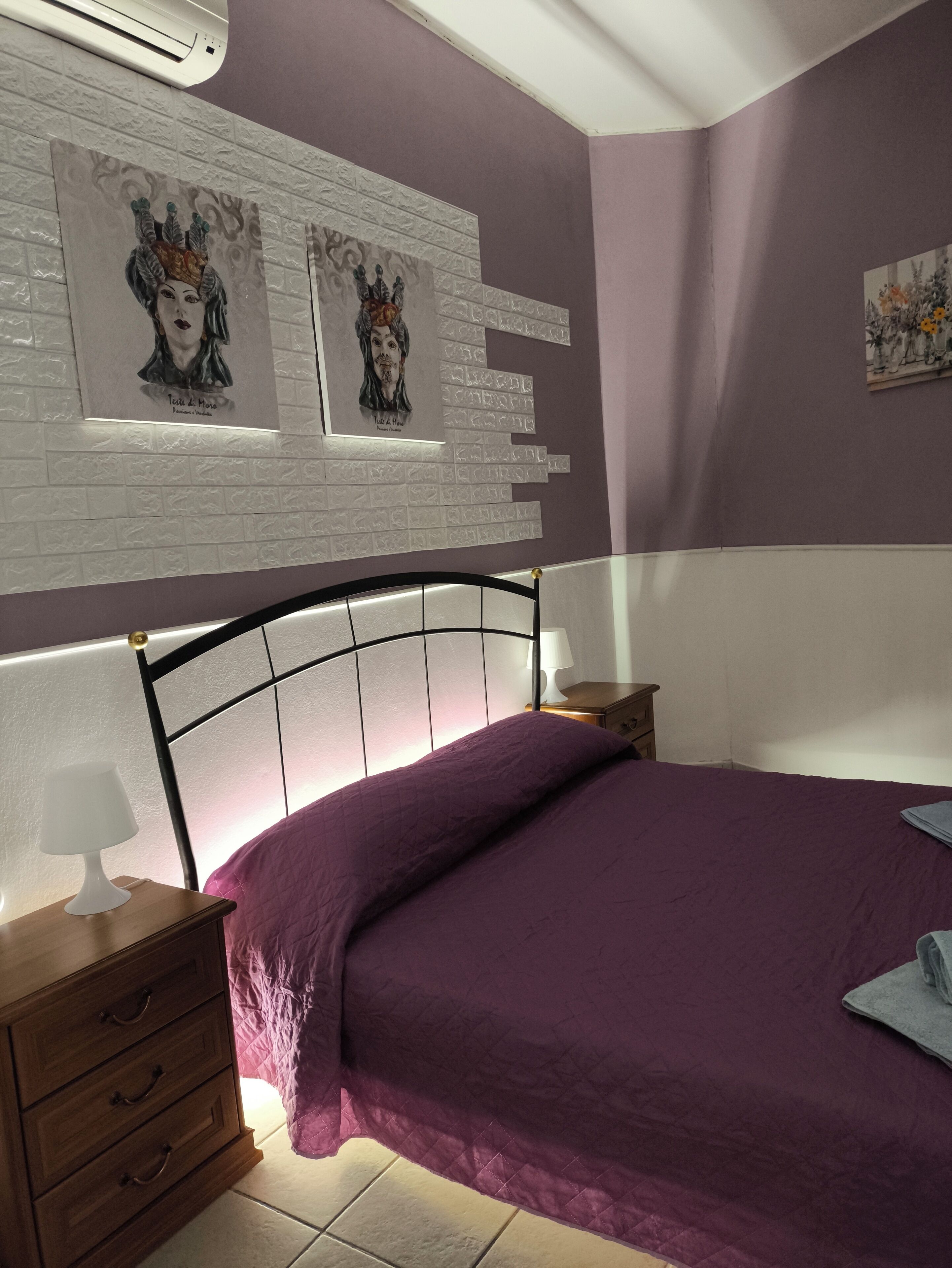 Un dormitorio con cama, mesita de noche, lámpara y decoración en la pared.