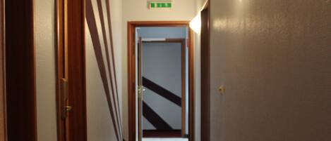 Un pasillo con alfombra roja, puertas de madera y una lámpara en la pared.