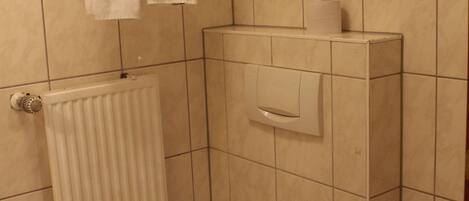 Un baño pequeño con inodoro, lavamanos, toallero con dos toallas, dispensador de papel higiénico y radiador.
