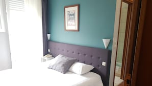 Una cama bien hecha con cabecera, una mesita de noche con lámpara y un cuadro en la pared.