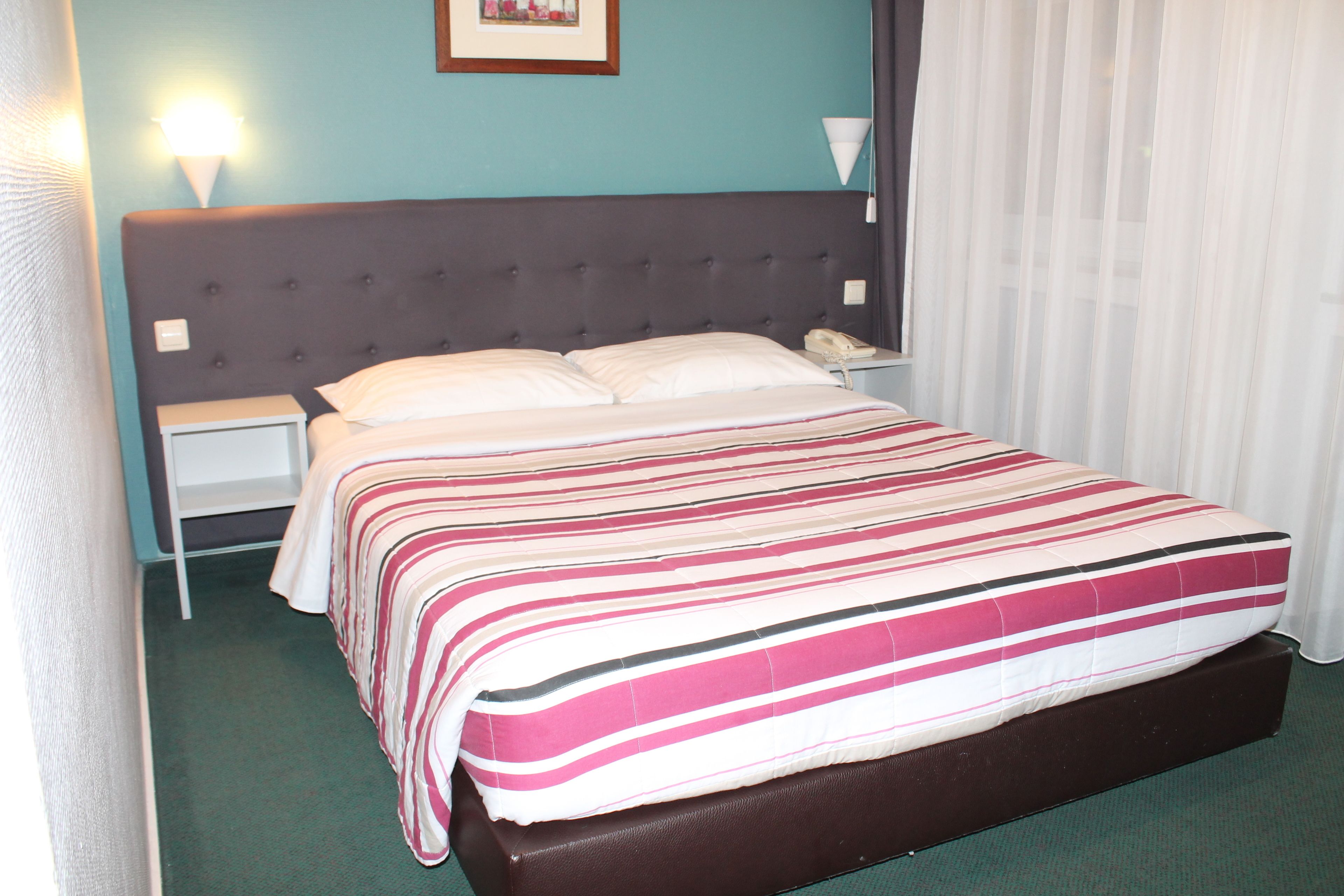 A hotel room with a bed, nightstands, a telephone, and a wall-mounted light fixture.