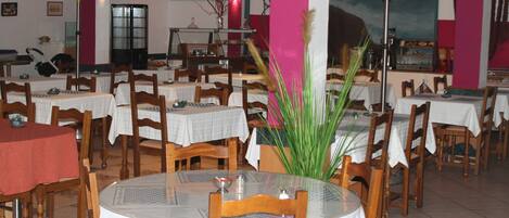 Un restaurante con mesas redondas, sillas de madera y una planta decorativa en el centro.