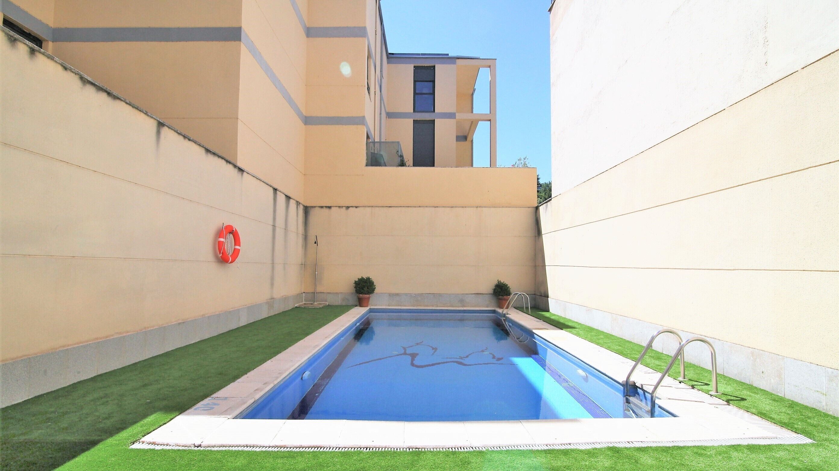 A swimming pool with a lifebuoy, surrounded by a low wall and artificial grass.