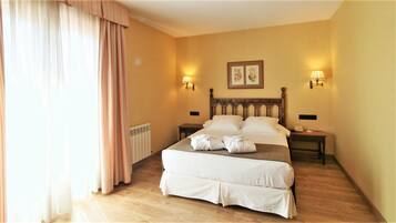A hotel room with a double bed, two bedside tables, a radiator, and a window with curtains.