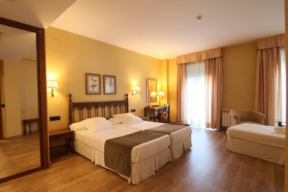 Une chambre d’hôtel avec deux lits, un bureau, une chaise et un grand miroir.