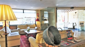 A hotel lobby with a sofa, armchairs, a table, a lamp, and a large decorative bowl. There is a sign for 'VISITAS PLAZA' and a QR code on the table. - Hotel Ele Puente Romano (Salamanca)