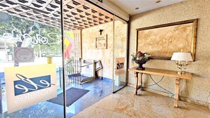 A reception area with a glass door, a reception desk, a wall-mounted lamp, and a framed artwork. - Hotel Ele Puente Romano (Salamanca)