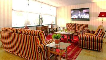 A living room with striped sofas, a glass coffee table, a TV, and a red lamp.