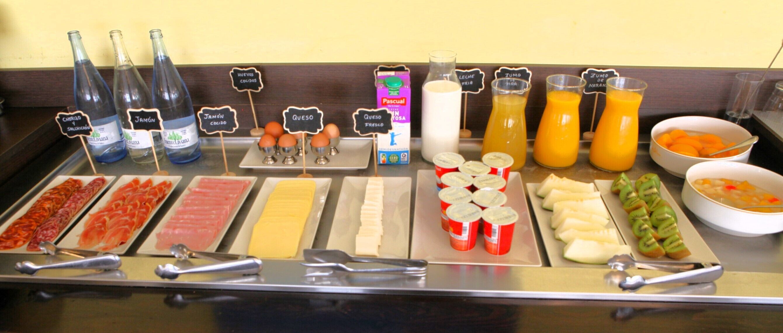 A buffet with various food items and beverages, including meats, cheeses, fruits, and juices.