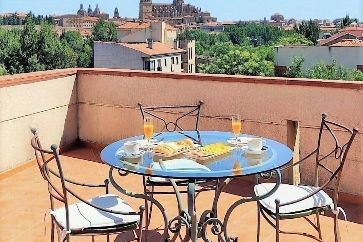 Une table ronde entourée de chaises, placée sur une terrasse, d’où l’on peut admirer un bâtiment historique doté de coupoles et de tours.