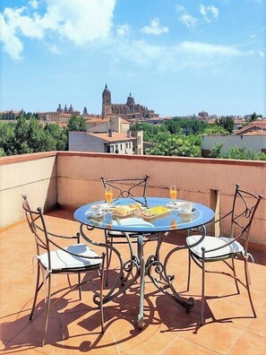 Eine Dachterrasse mit einem runden Tisch und Stühlen, einem Frühstücksaufenthalt und Blick auf ein historisches Gebäude im Hintergrund.