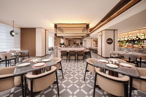 Un comedor moderno con varias mesas y sillas, una zona de bar central y un suelo estampado.