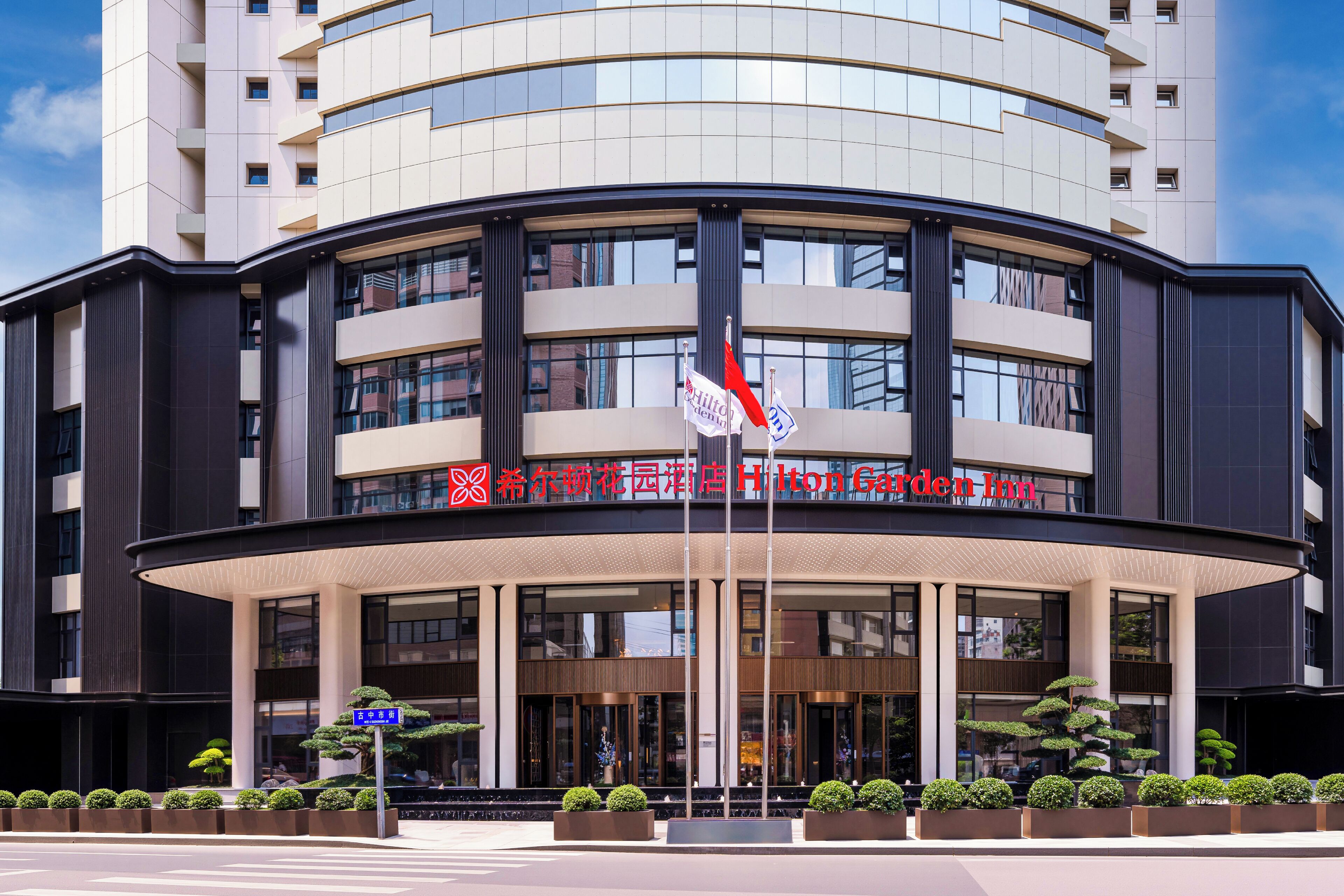 Ein modernes Hotel mit einer geschwungenen Fassade, mehreren Etagen und einem gut sichtbaren Hilton Garden Inn Schild.