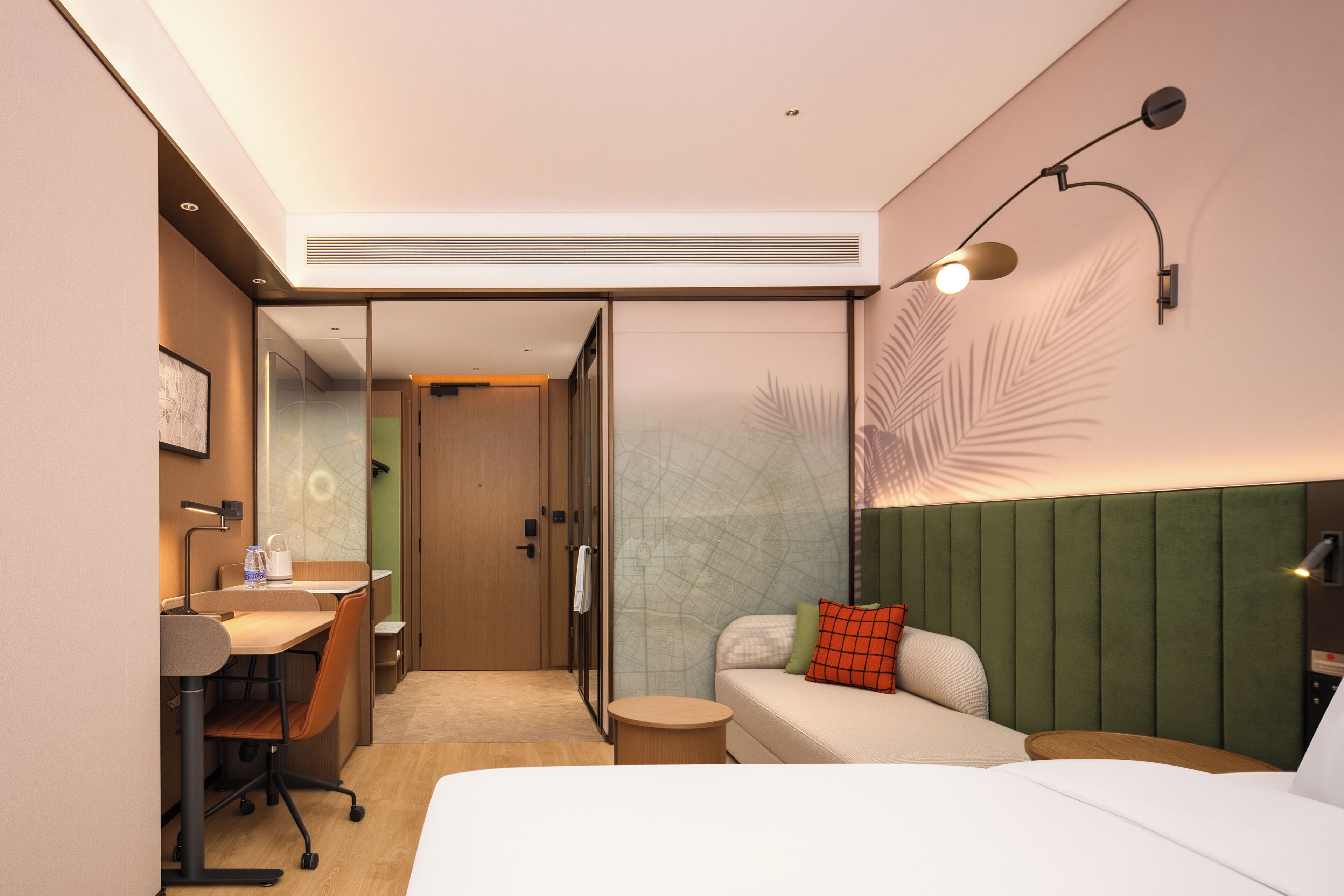 A hotel room with a bed, a sofa, a desk with a chair, a small round table, and a wall-mounted lamp.