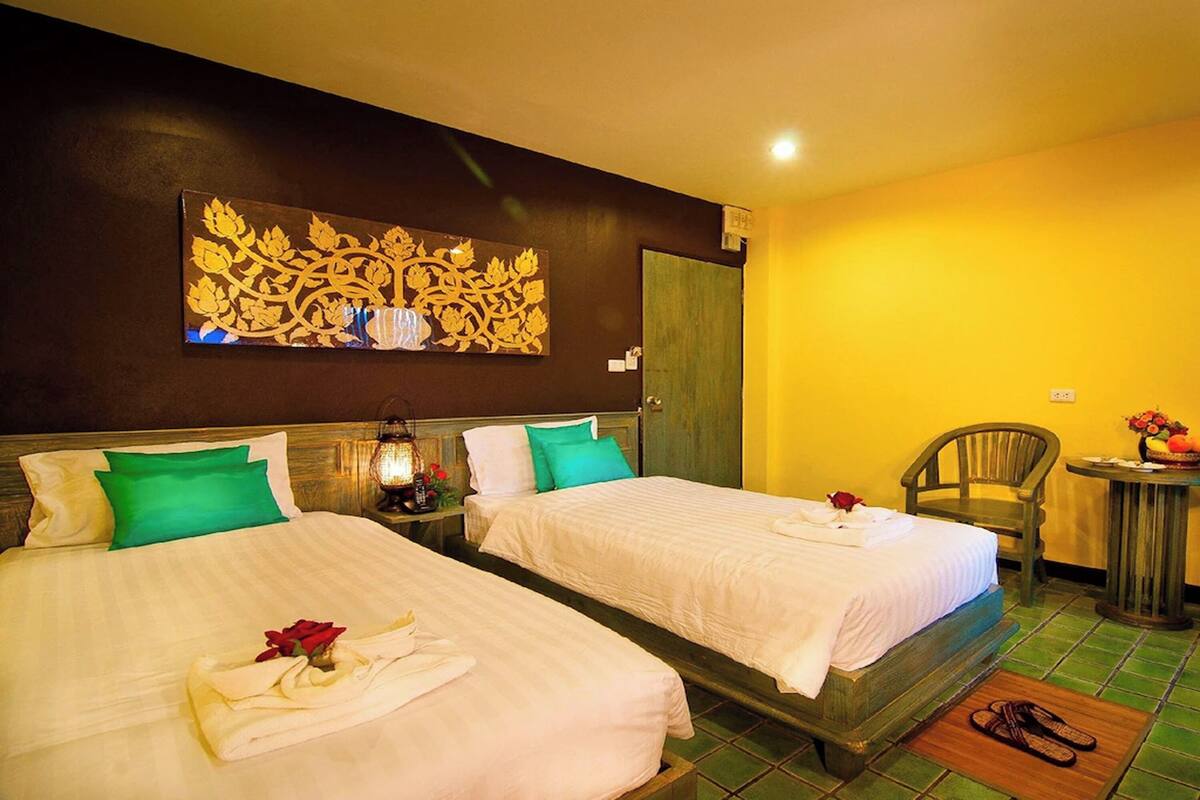 A hotel room with two beds, a nightstand with a lamp, a chair, and a small table with a fruit bowl.