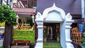 A boutique hotel entrance with a green artificial lawn, a wooden bench, and a sign reading "CM Night Boutique Hotel".