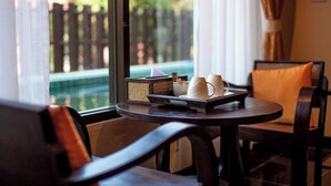 A dining area with a table set for two, featuring a tray with two white cups and a small bowl. The room has a view of a pool and a wooden fence outside.