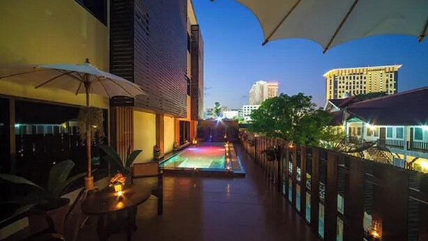 An outdoor pool area with umbrellas, a pool, and a view of buildings in the background.