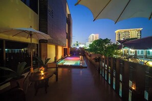 An outdoor pool area with umbrellas, a pool, and a view of buildings in the background. - CM Night Bazaar Boutique Hotel (Chiang Mai)