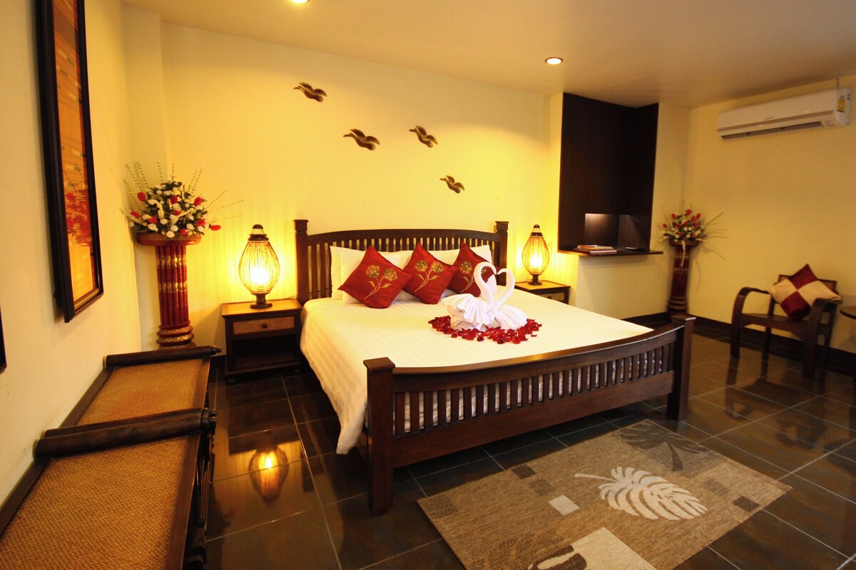 Habitación de hotel impecable con una cama grande, un espacio de descanso con una silla y una mesa, y un televisor montado en la pared.