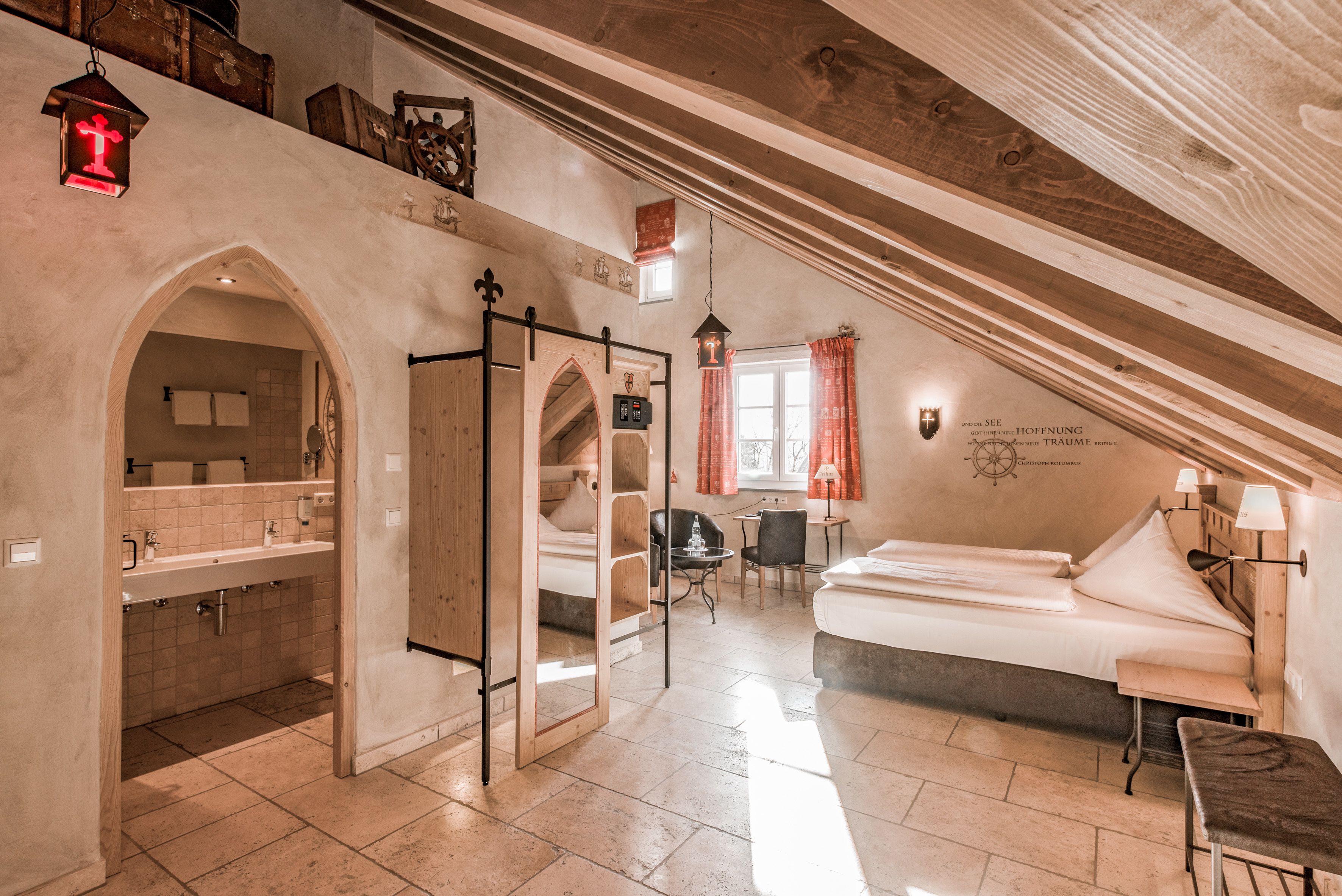 A room with a bed, a desk, a chair, and a bathroom with a sink and mirror.