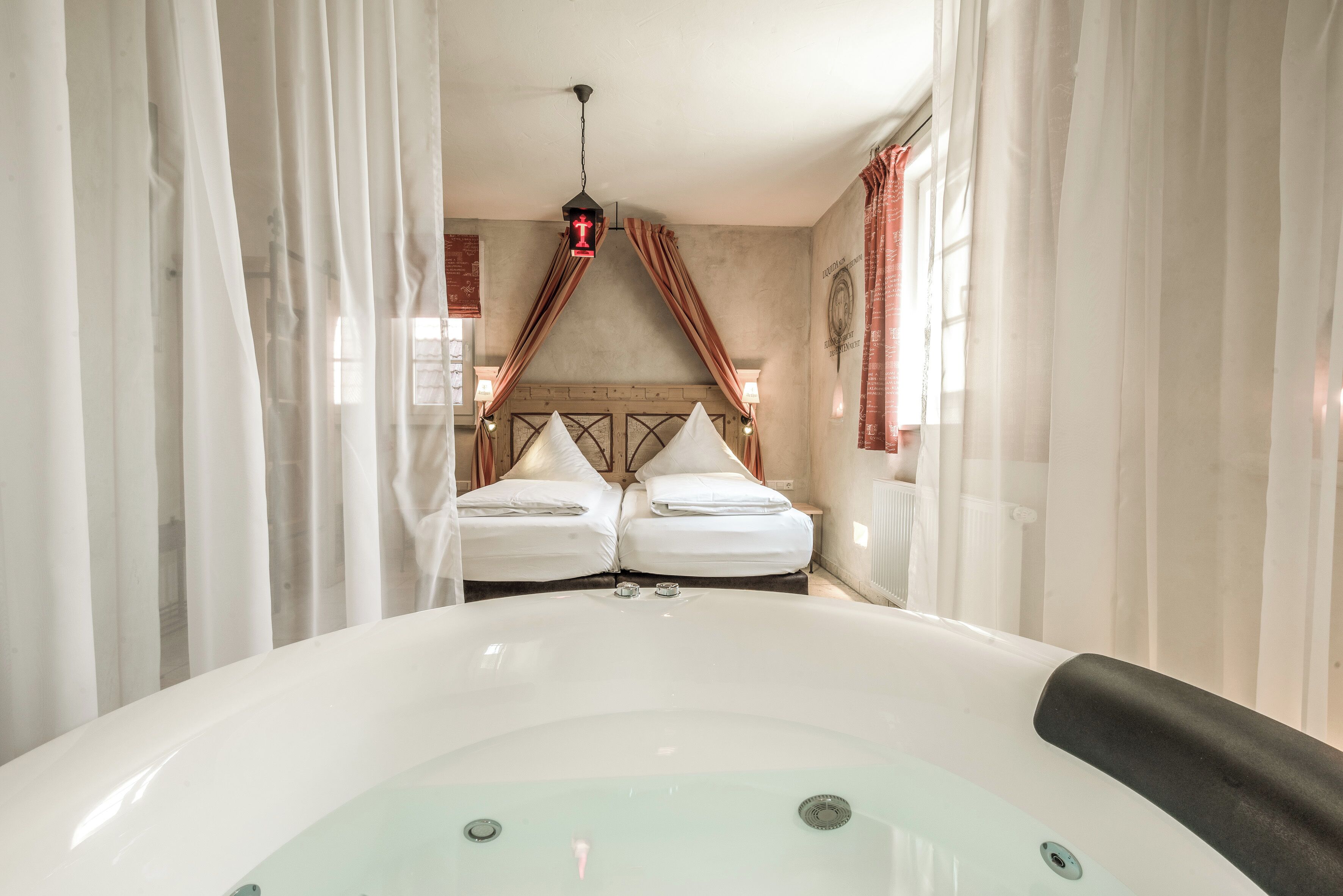 A room with a large bathtub, two beds with white linens, and a wooden headboard.