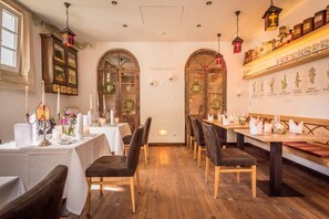 L’intérieur d’un restaurant avec des tables en bois, des chaises sombres et une ambiance tamisée à la lumière des bougies.