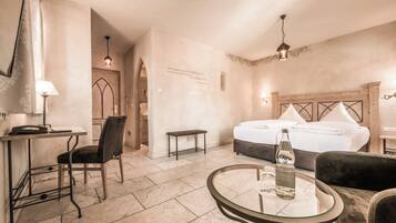 A hotel room with a bed, a desk with a chair, a small table, and a lamp.