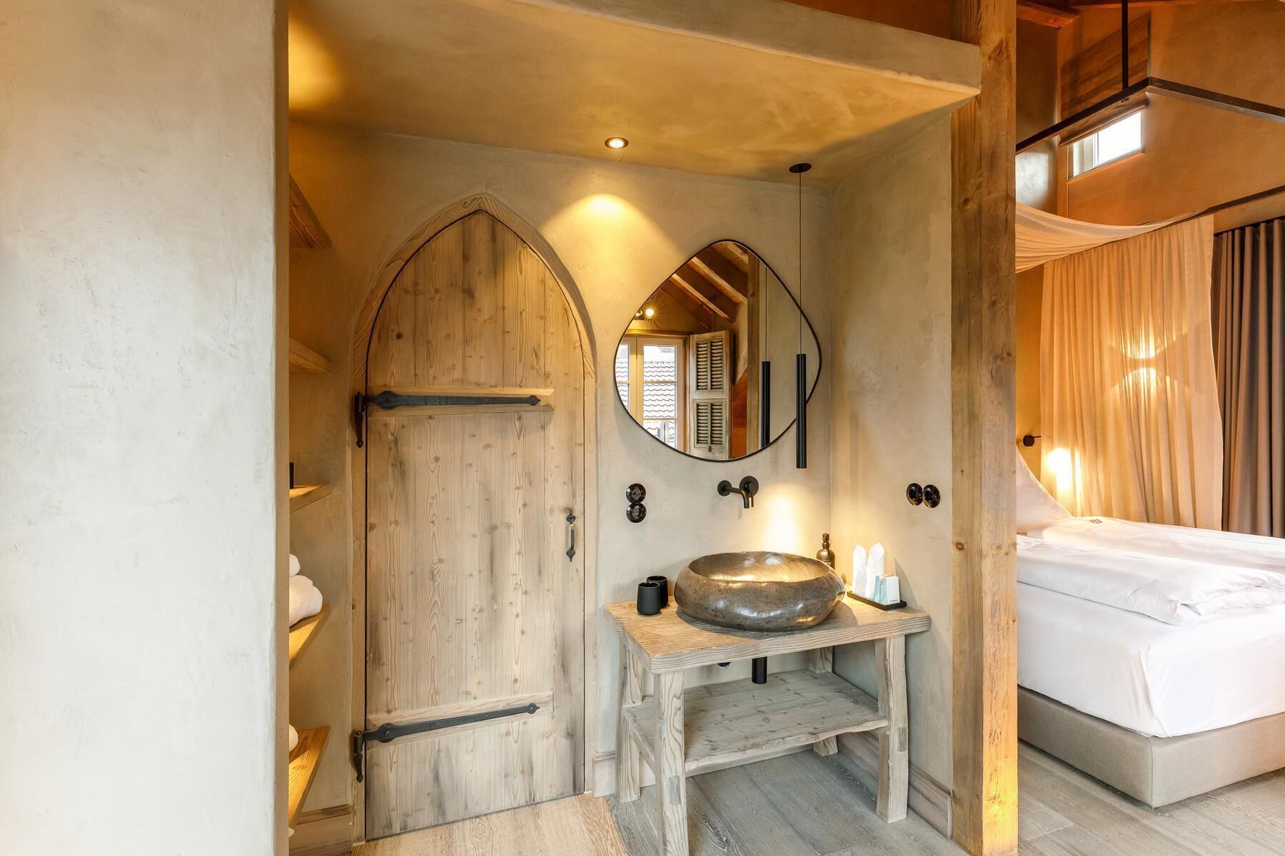Un baño rústico con una puerta de madera, un espejo redondo y un lavabo con una pileta grande.