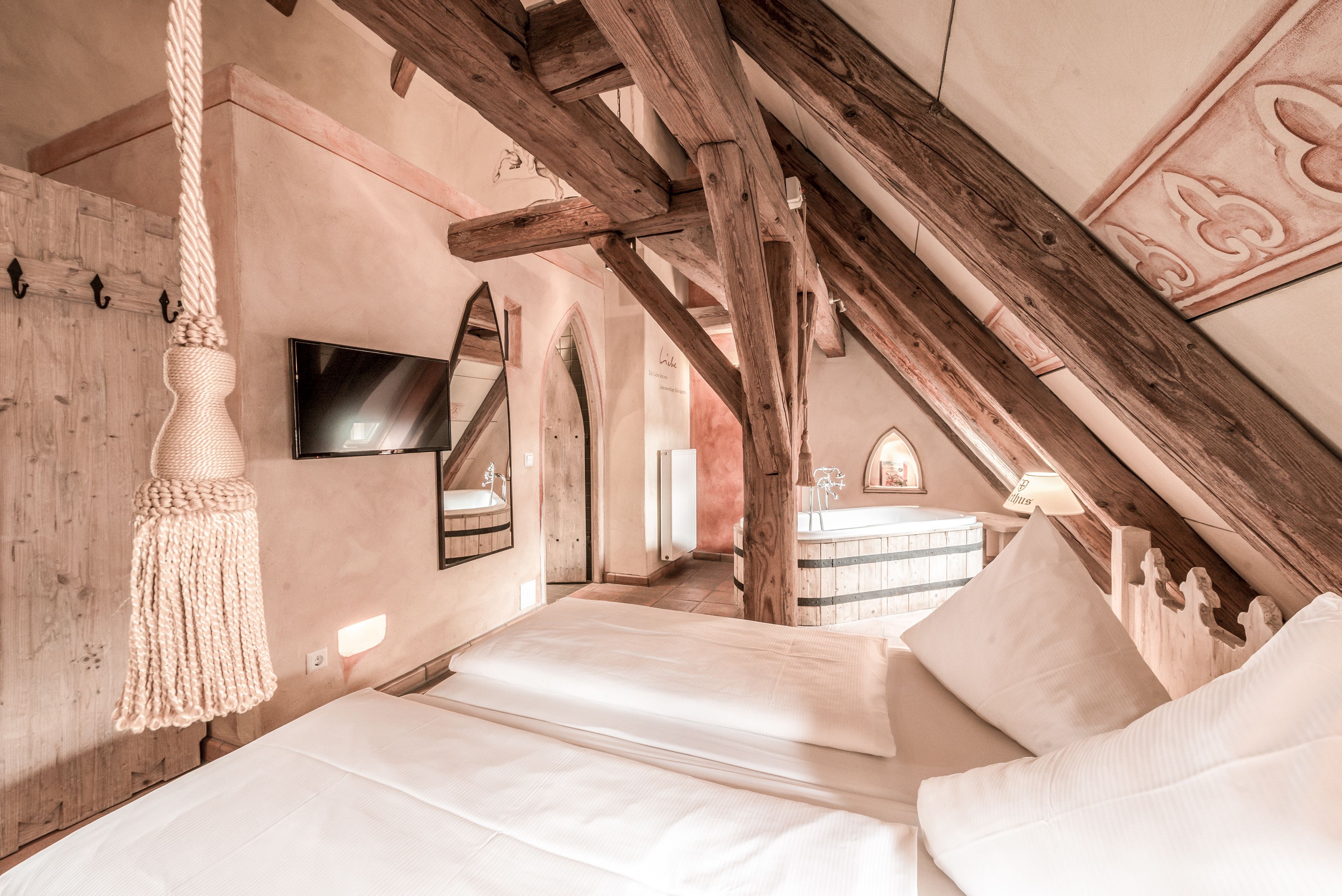Une chambre avec un plafond en bois, un lit, une lampe suspendue et un téléviseur fixé au mur.