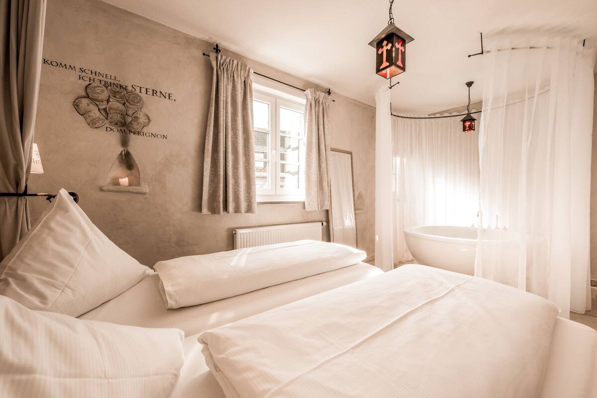 A hotel room with a large bed, a bathtub, and a window with curtains.