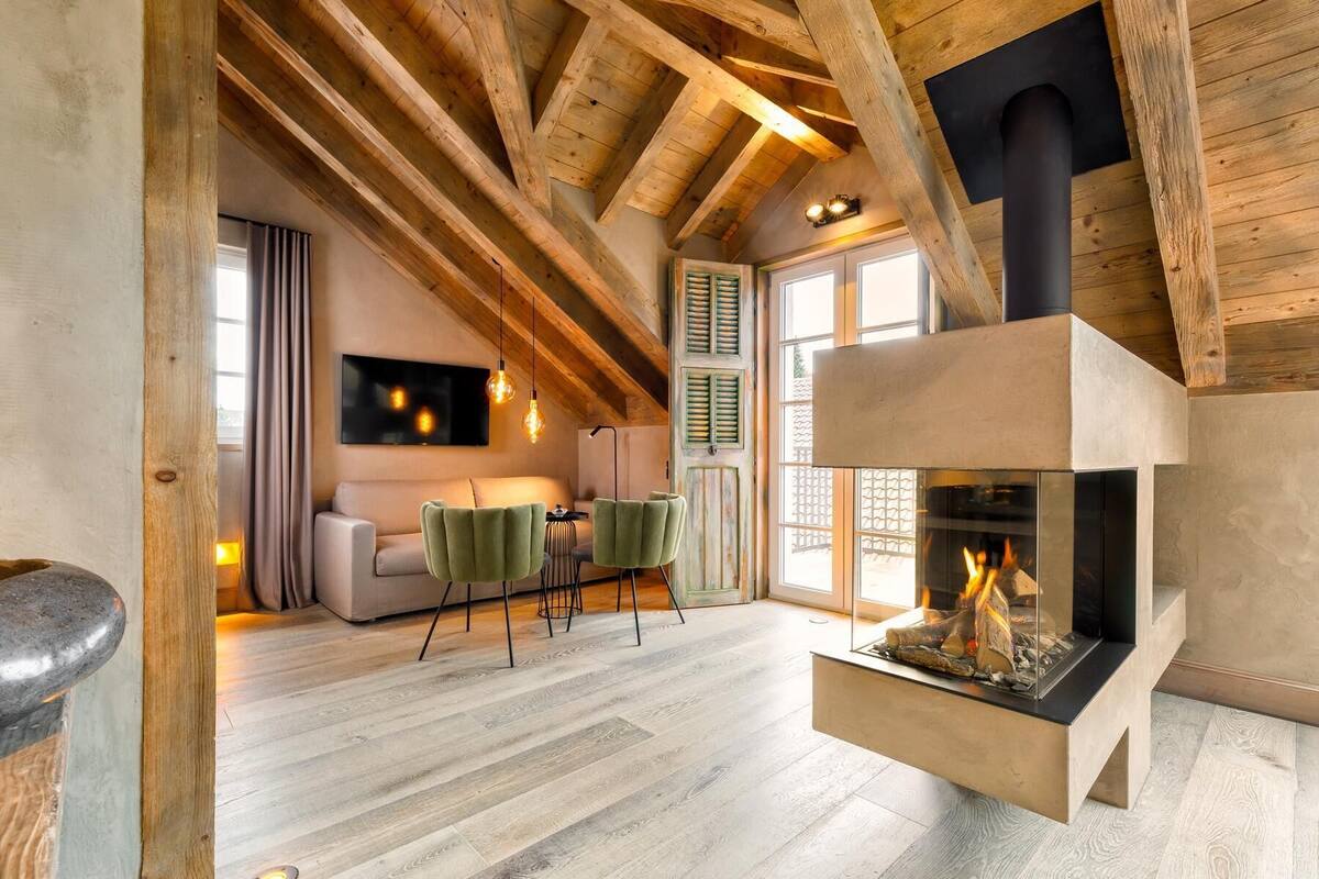 A rustic interior with exposed wooden beams, a fireplace, a sofa, and a dining area.
