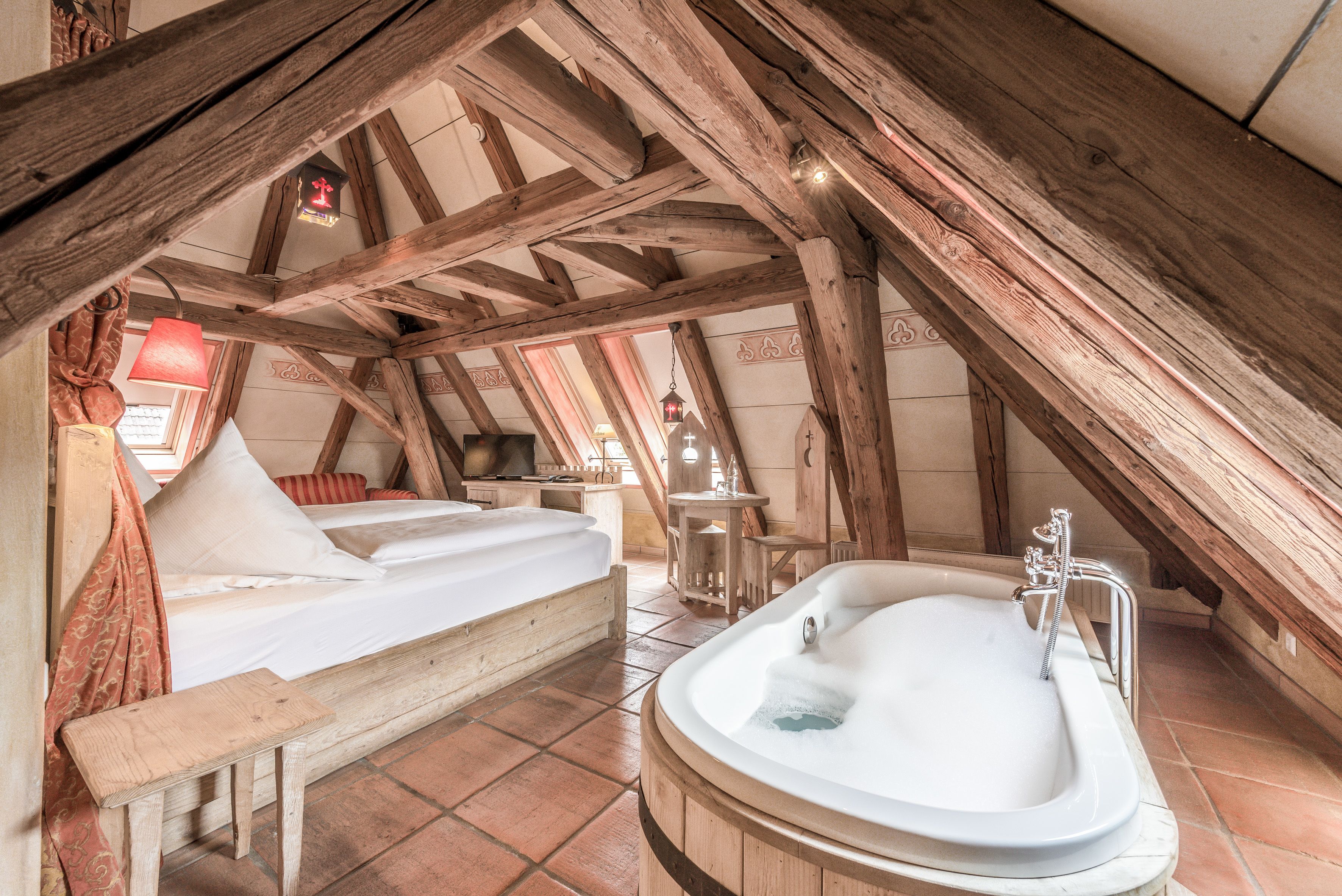 A cozy attic bedroom with a wooden bed, a large bathtub, and a sloped ceiling.