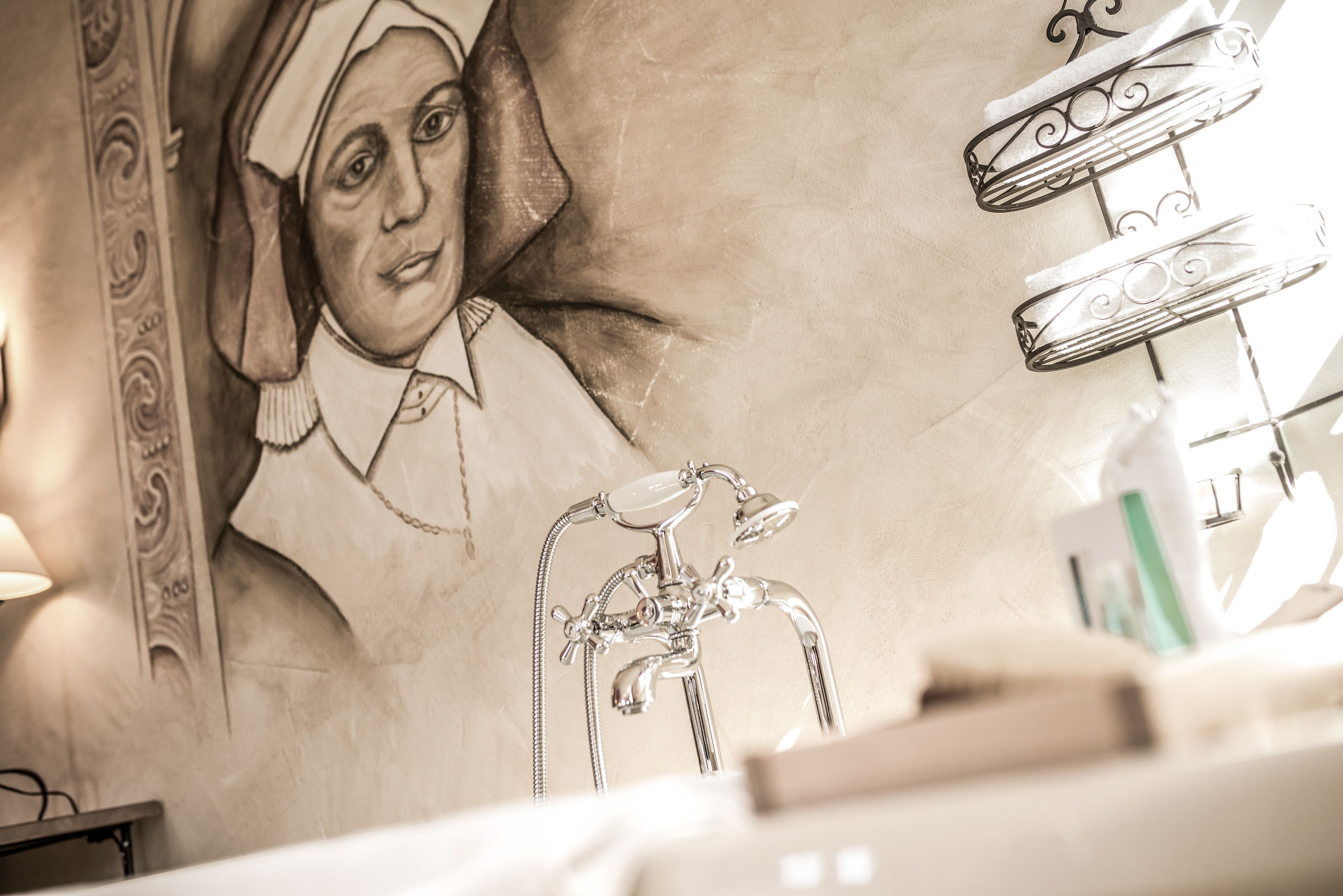 Un baño con un mural de una figura histórica, una bañera clásica y una ducha moderna.