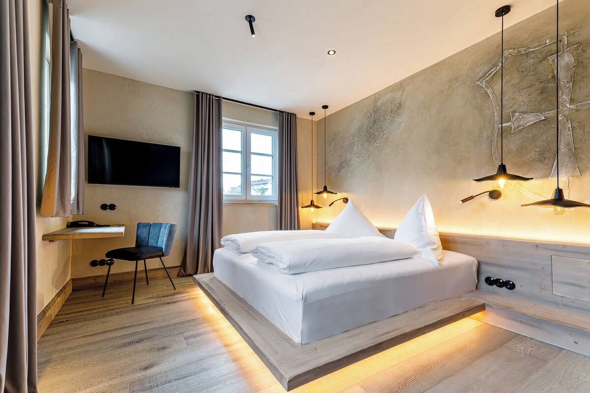 A modern bedroom with a bed, a desk, a chair, and a TV mounted on the wall.