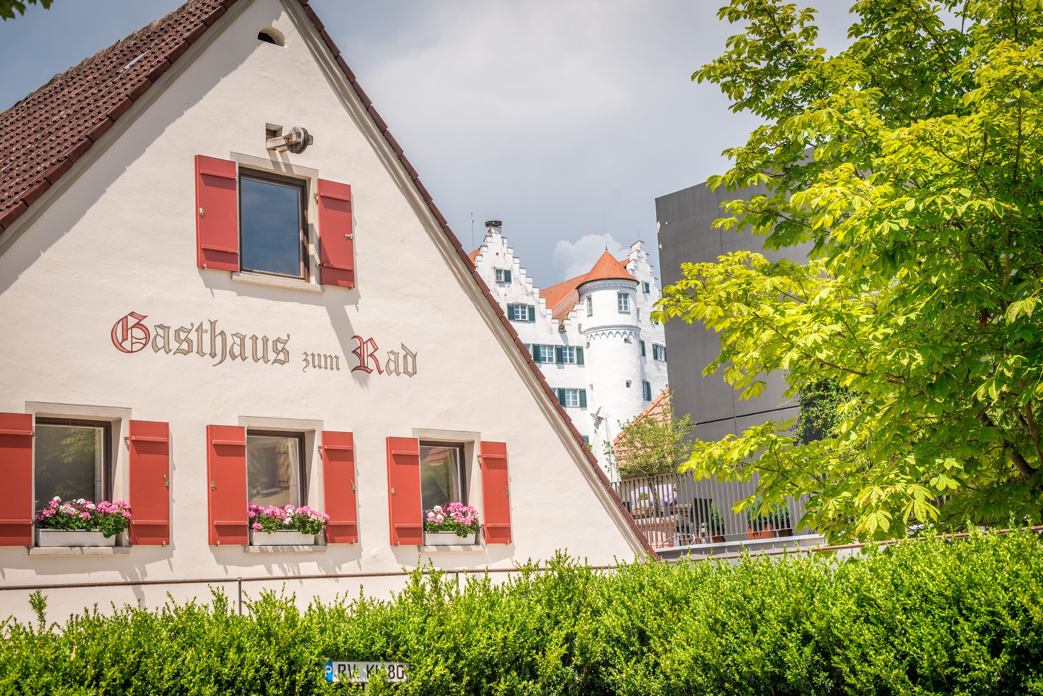 Ein Gebäude mit der Beschilderung "Gasthaus zum Rad" und roten Fensterläden, umgeben von viel Grün.