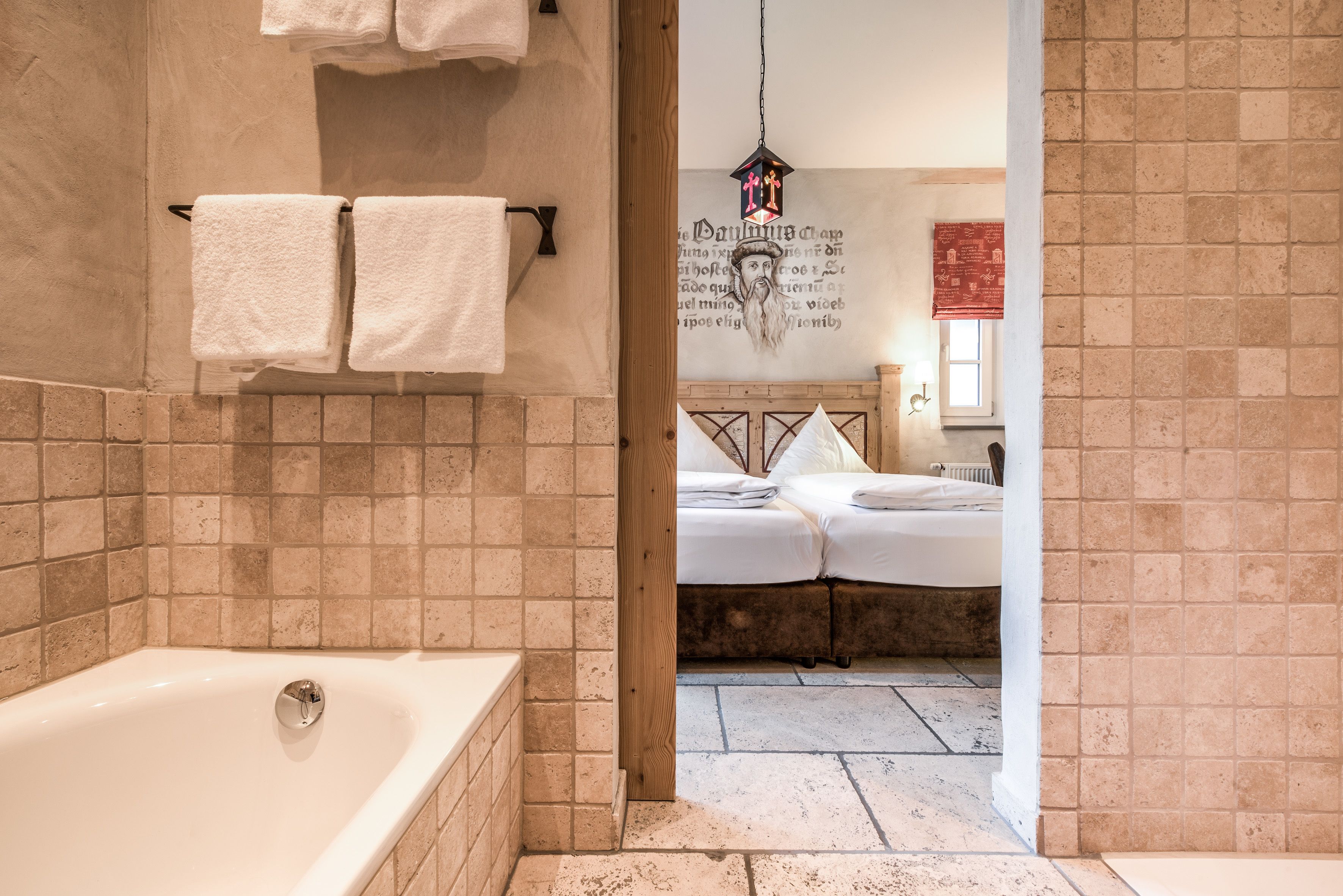 A bathroom with a bathtub, two towels hanging on a rack, and a bed visible through an open doorway.