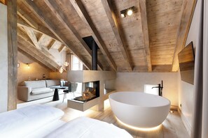 A modern interior with exposed wooden beams, a large white bathtub, a sofa, and a fireplace. - Hotel Arthus (Aulendorf)