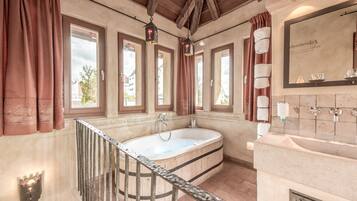 A bathroom with a bathtub, a sink, and a mirror. There are windows with curtains and a wooden ceiling.
